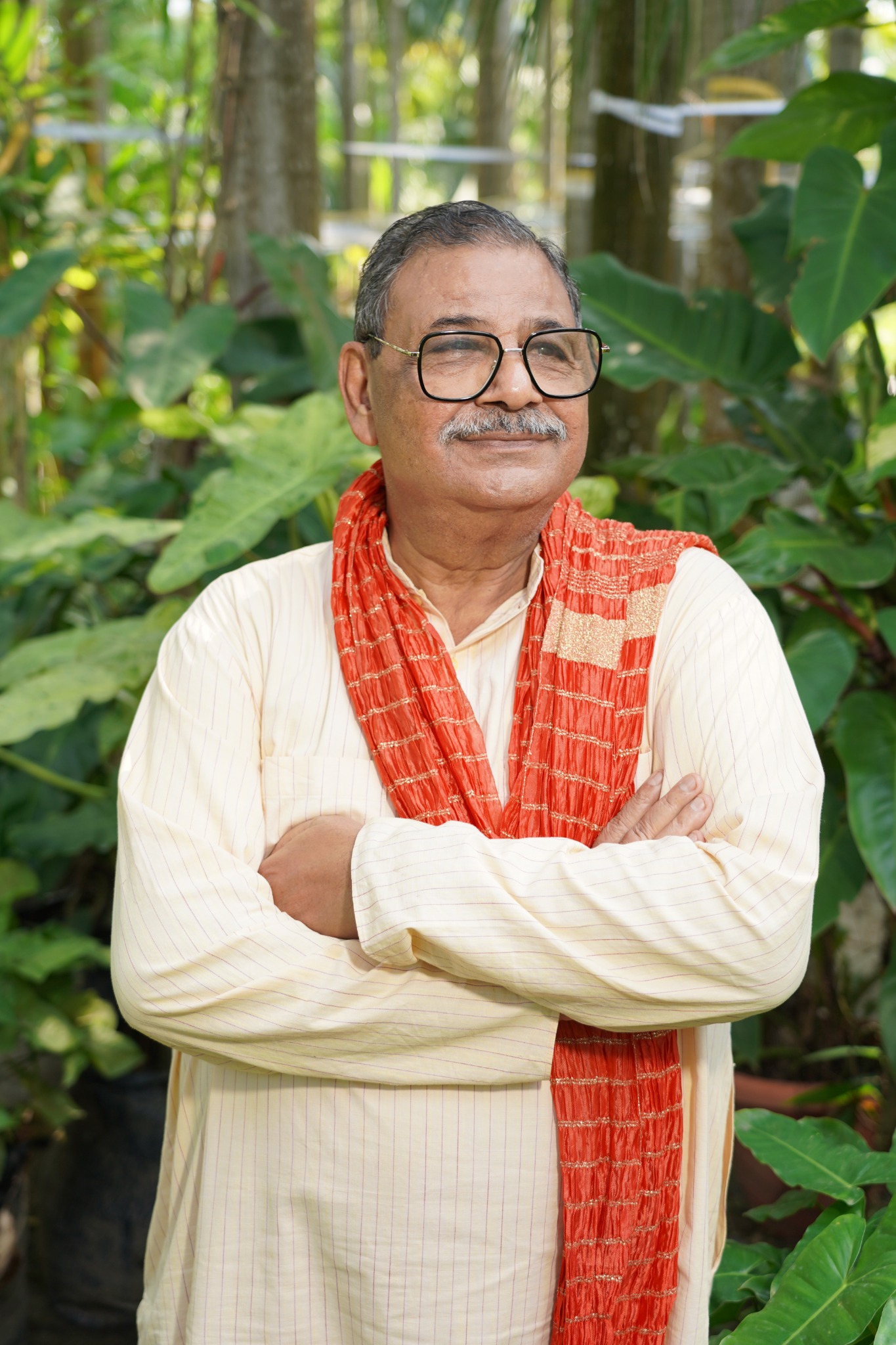 Dinesh Chandra Rawat standing in a garden, wearing a cream kurta and saffron scarf